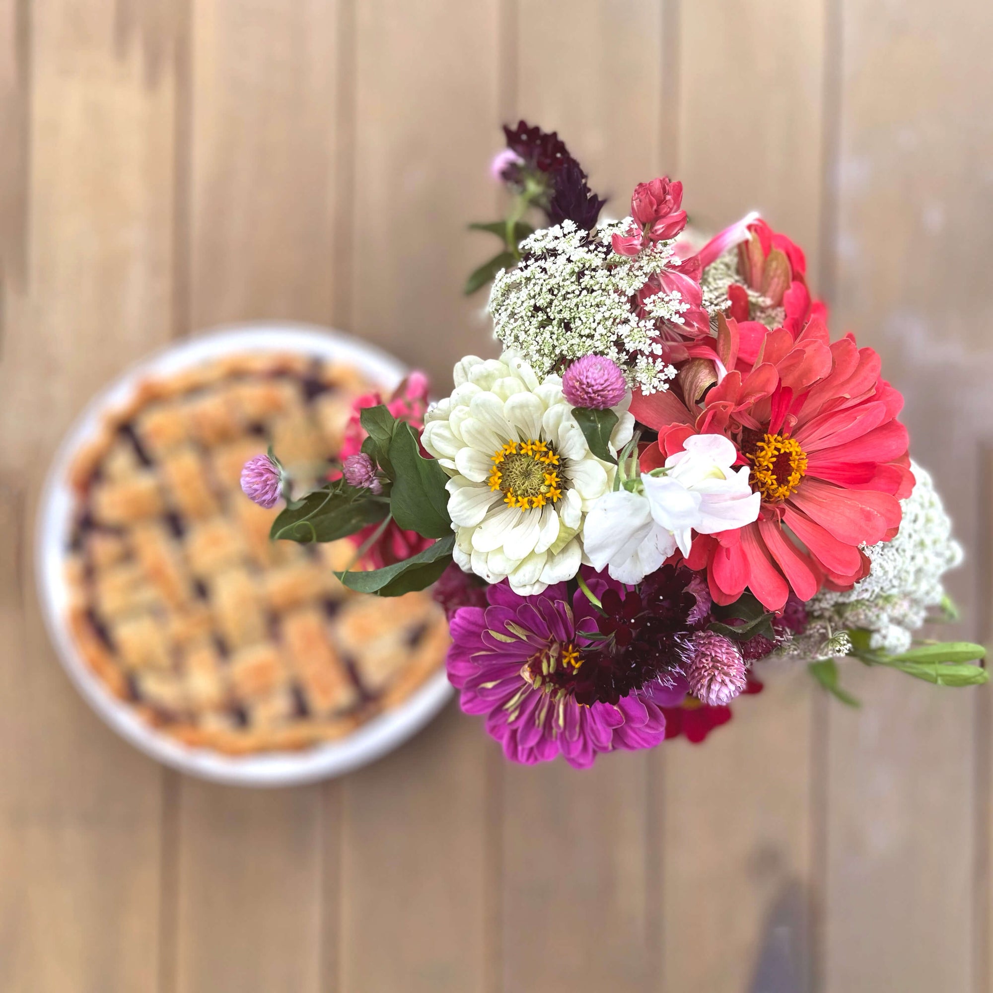 Bouquet of colorful flowers in front of a pie on a wooden surface.