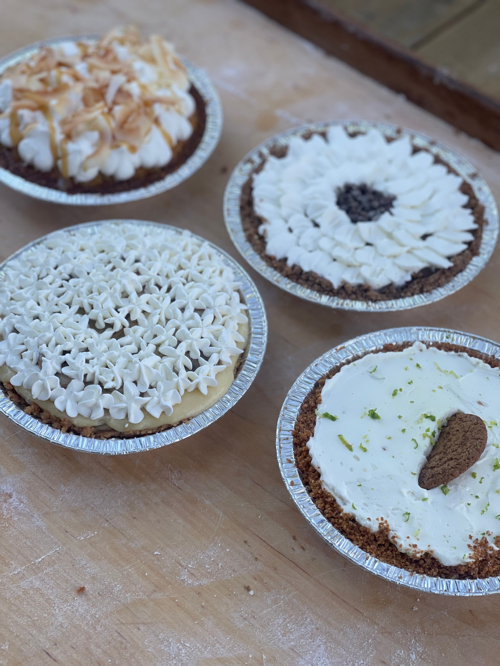 Four small cream pies with different toppings on a wooden surface